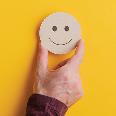 Hand holding a smiley face on a yellow background
