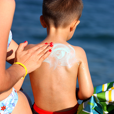 Mother putting sunscreen on their sons back