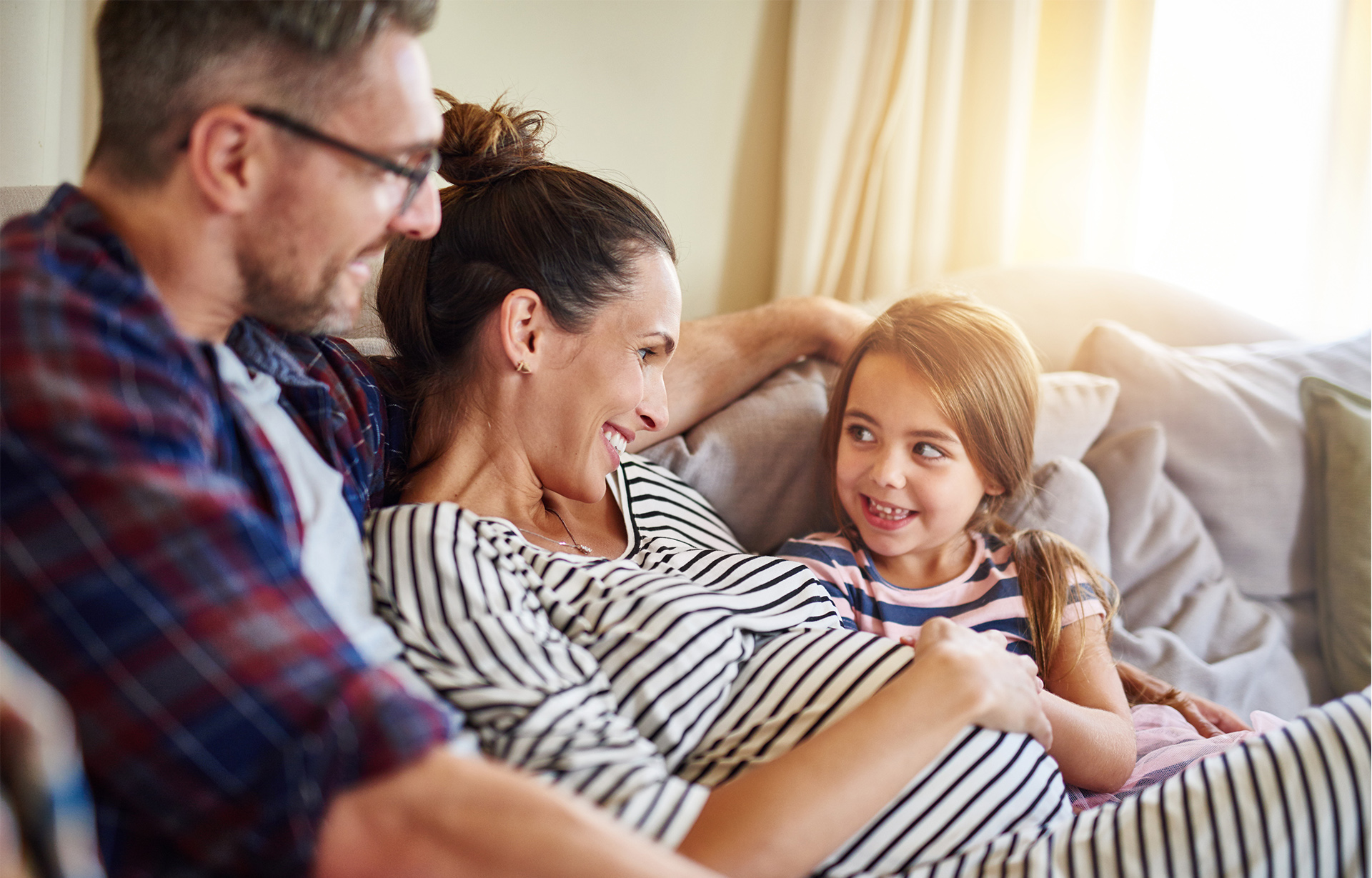 Man and pregnant woman sitting on couch with daughter